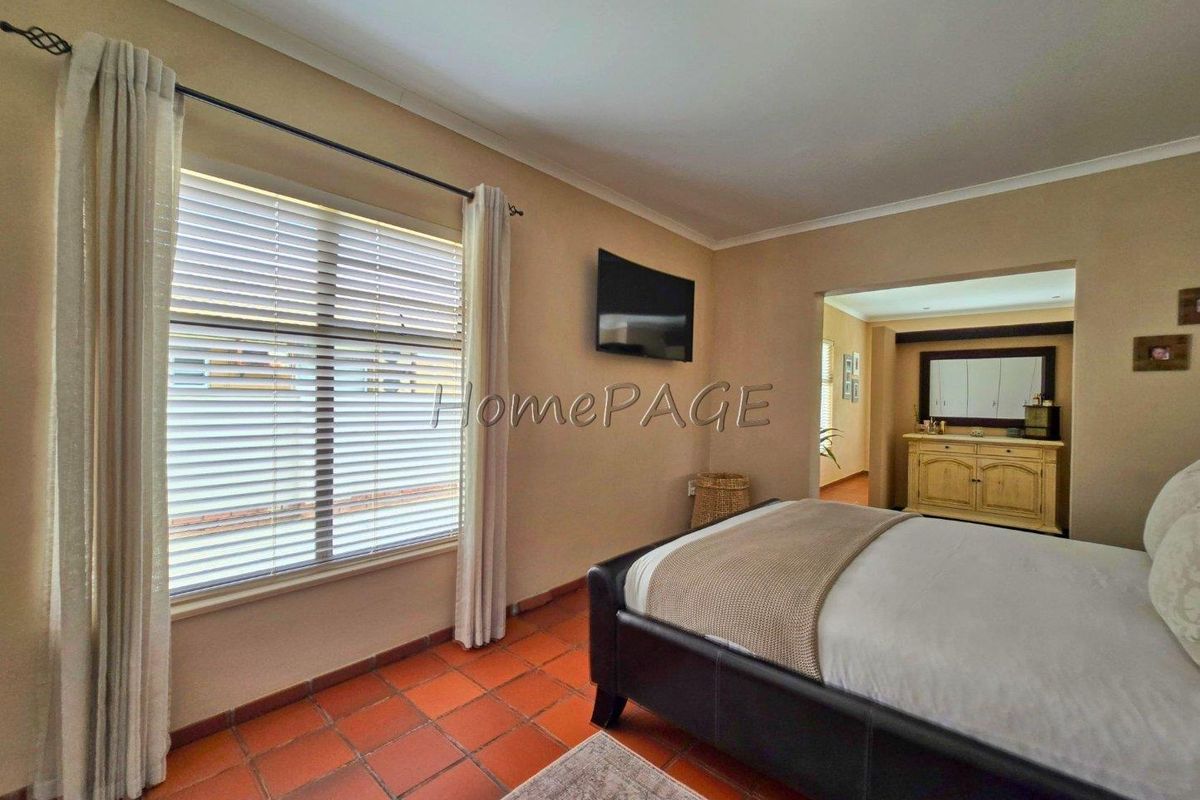 A bedroom featuring terracotta floor tiles, neutral wall tones, and an adjoining space, providing a comfortable and functional living area.