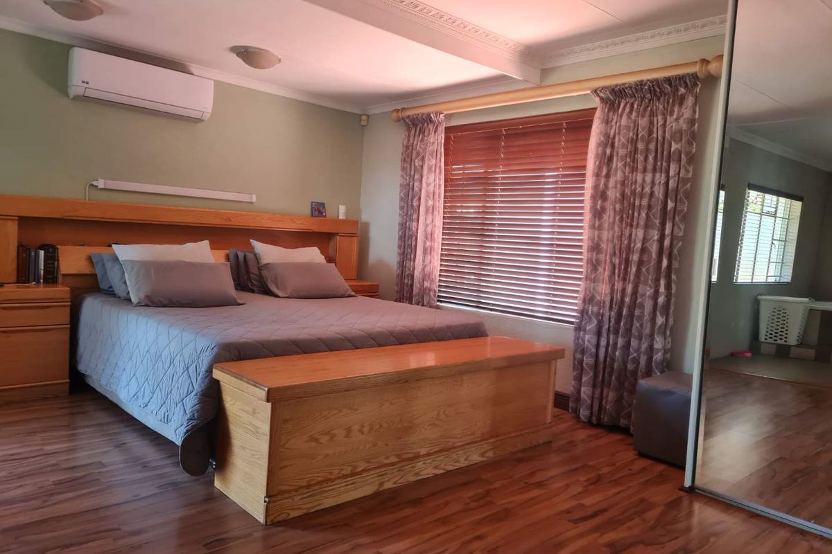 Spacious bedroom featuring laminate flooring, built-in headboard, air conditioning unit, and large mirrored sliding wardrobe doors.