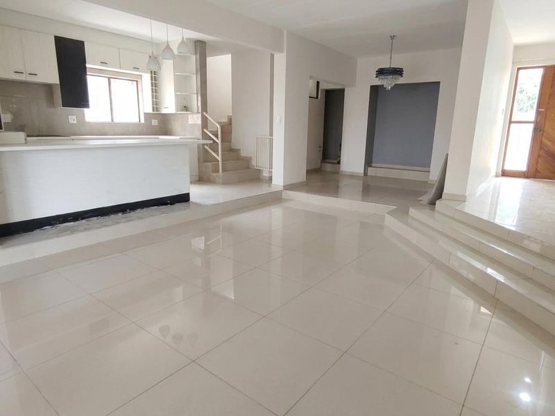Spacious open-plan living and kitchen area featuring large format floor tiles, a modern kitchen island, and a split-level layout with a staircase.