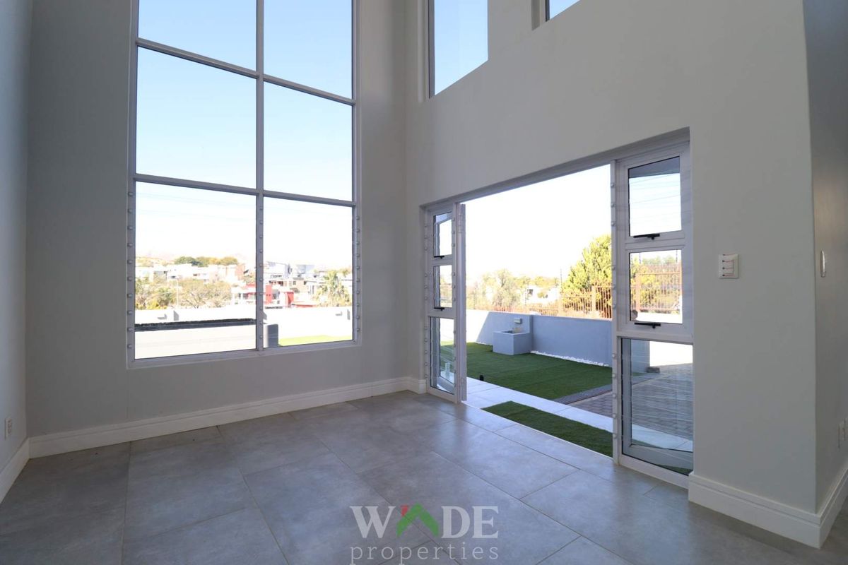 Spacious living area featuring double-volume ceilings, large floor-to-ceiling windows, and seamless access to an outdoor patio area.