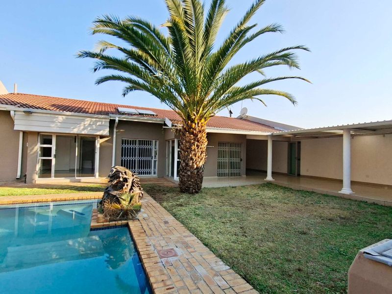 Rear exterior view featuring a swimming pool, covered patio area, and established garden with a large palm tree.