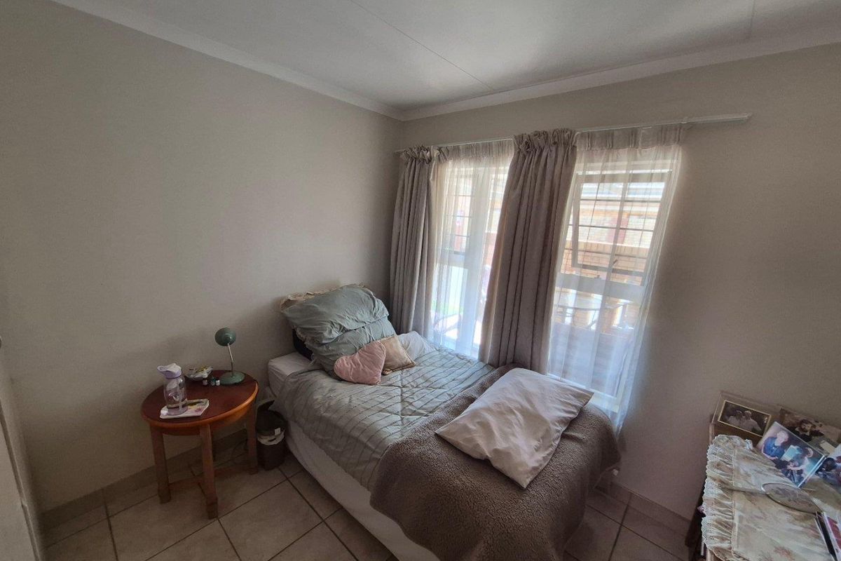 A compact bedroom featuring neutral wall tones, tiled flooring, and large windows with curtain tracks, providing natural light.