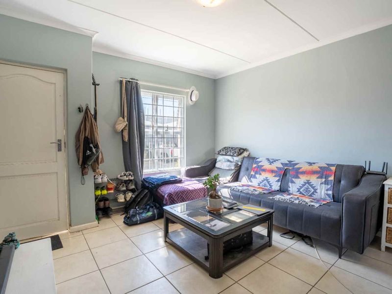 A living room featuring tiled flooring, a window with security bars, and a standard door, providing a functional and well-lit living space.