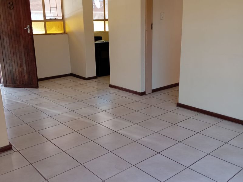 An empty living area featuring neutral tiled flooring, textured ceilings, and timber door access, providing a blank canvas for interior design updates.