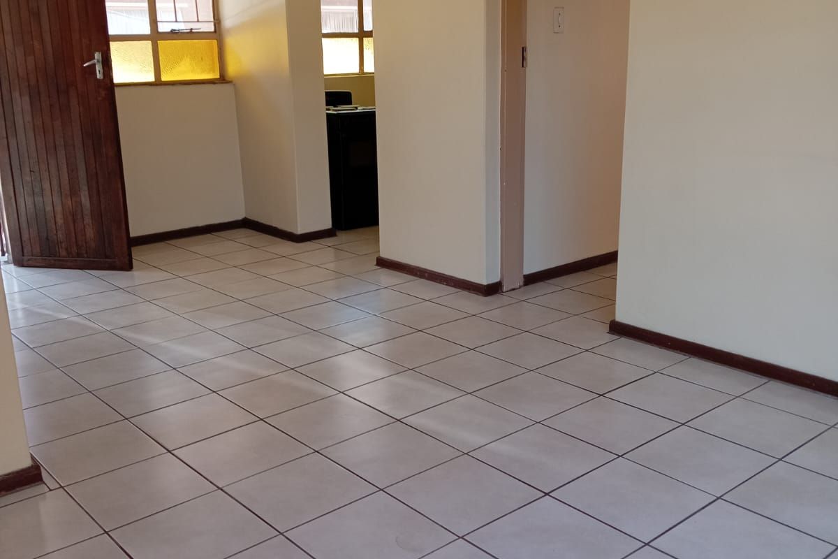 An empty living area featuring neutral tiled flooring, textured ceilings, and timber door access, providing a blank canvas for interior design updates.