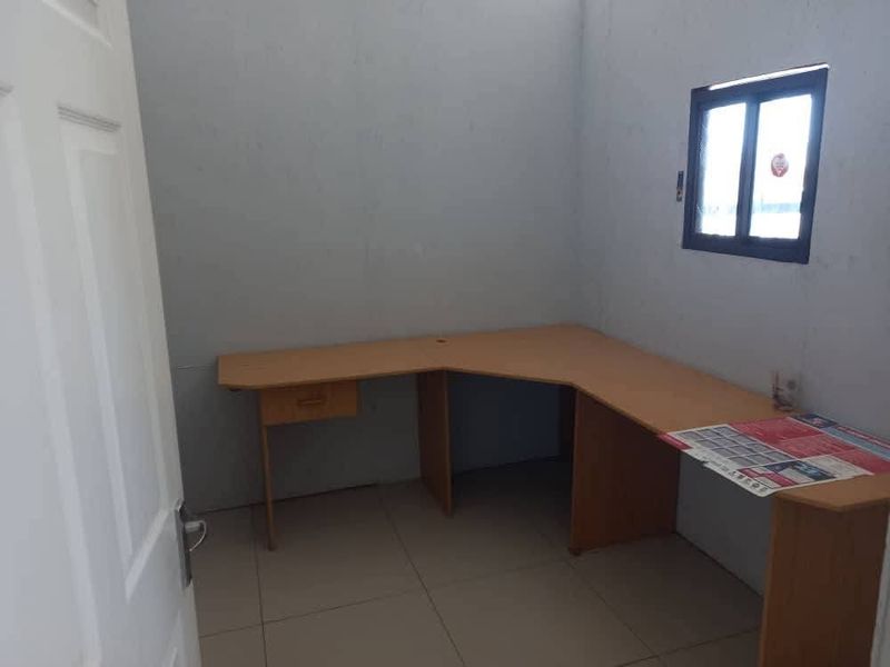 A functional office space featuring tiled flooring, a built-in corner desk, and a window providing natural light.