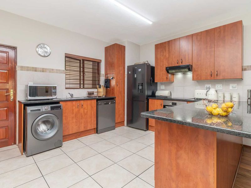 A functional kitchen featuring wood-finish cabinetry, granite countertops, tiled flooring, and a tiled backsplash, providing a practical workspace for daily cooking and laundry needs.