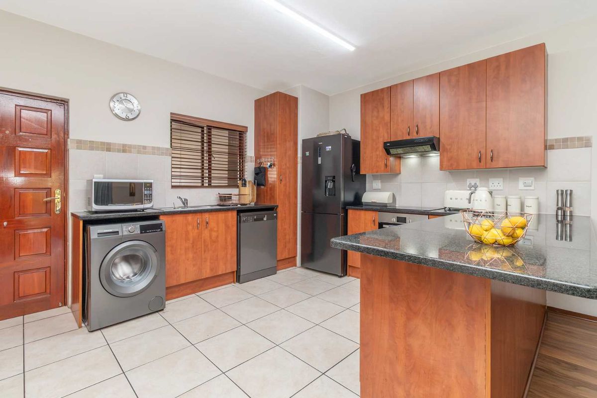 A functional kitchen featuring wood-finish cabinetry, granite countertops, tiled flooring, and a tiled backsplash, providing a practical workspace for daily cooking and laundry needs.