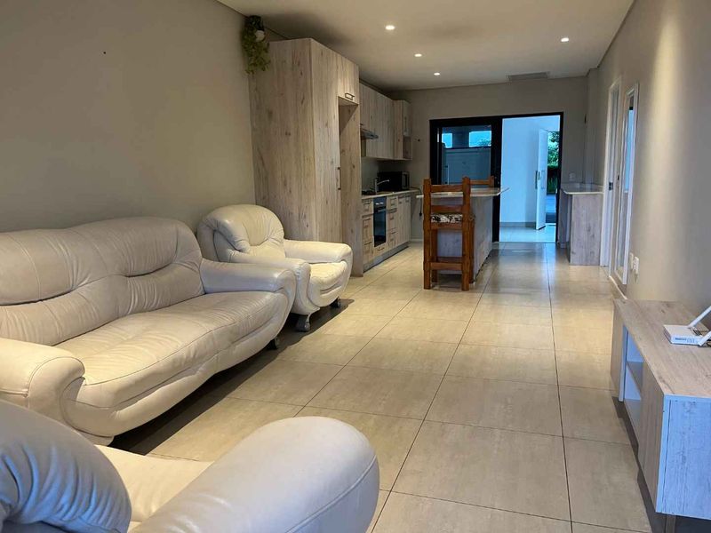 Open-plan living area featuring a modern kitchen with built-in cabinetry, integrated appliances, and a central island, flowing into a spacious lounge with tiled flooring.