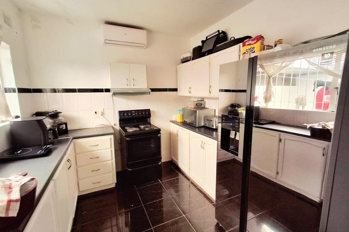 A functional kitchen featuring white built-in cabinetry, dark laminate countertops, a black electric stove, and tiled flooring with a wall-mounted air conditioning unit.