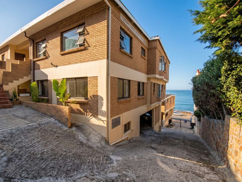 Exterior view of a multi-story brick apartment building featuring a concrete driveway, undercover parking, and ocean views.