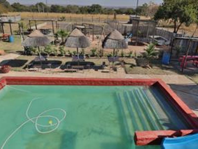 Outdoor pool area featuring a swimming pool with a slide, paved surround, and multiple thatched umbrellas set within a spacious garden environment.