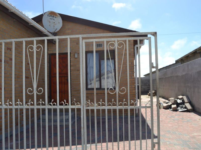 Front view of a face brick house featuring a paved driveway, secure metal gate, and boundary wall.