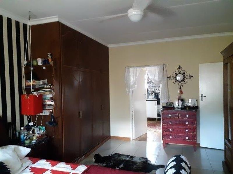 A bedroom featuring built-in wooden cupboards, tiled flooring, and a ceiling fan, with an adjoining room visible through the doorway.