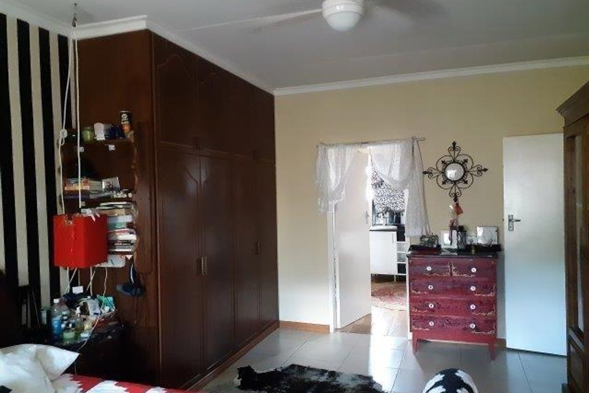 A bedroom featuring built-in wooden cupboards, tiled flooring, and a ceiling fan, with an adjoining room visible through the doorway.