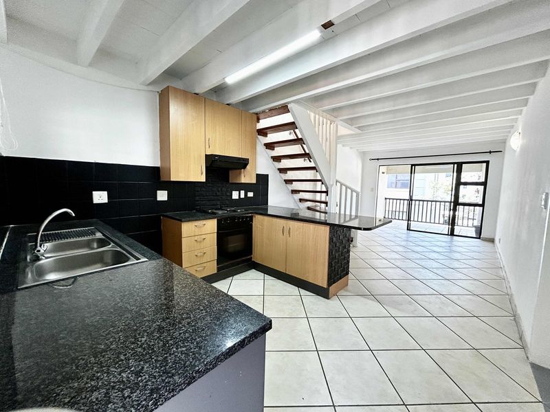 Open-plan kitchen and living area featuring tiled floors, exposed beam ceilings, built-in cabinetry, and direct access to a balcony via sliding glass doors.