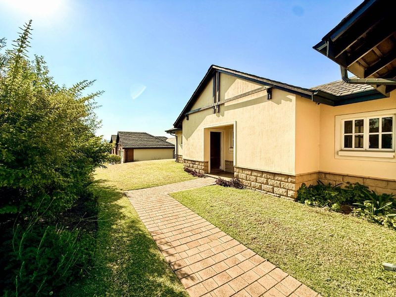 A well-maintained rear exterior view featuring a paved walkway leading to the house, stone cladding accents, and a neat lawn area.