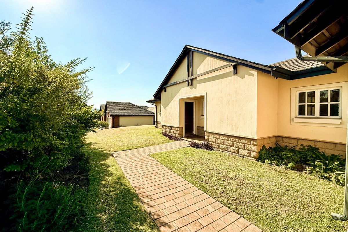 A well-maintained rear exterior view featuring a paved walkway leading to the house, stone cladding accents, and a neat lawn area.