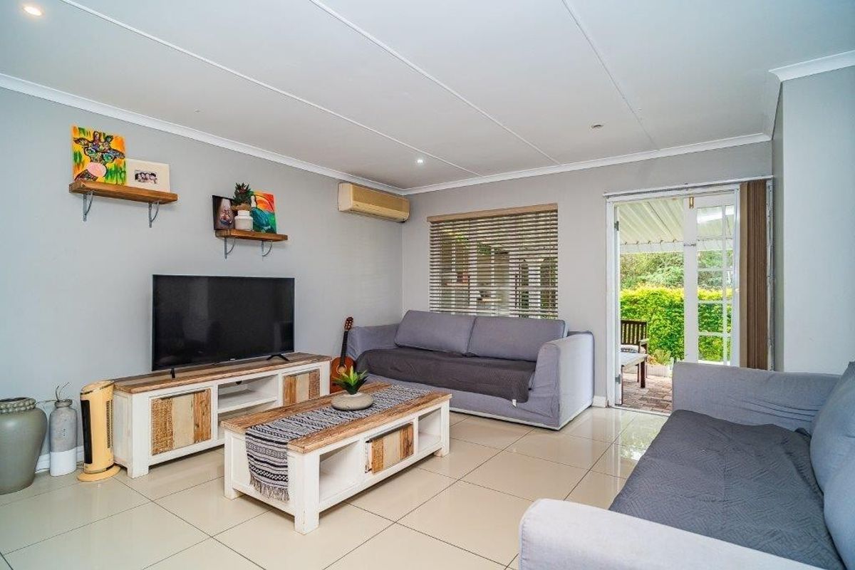 A bright living room featuring tiled flooring, a wall-mounted air conditioning unit, and direct access to an outdoor patio area through sliding glass doors.