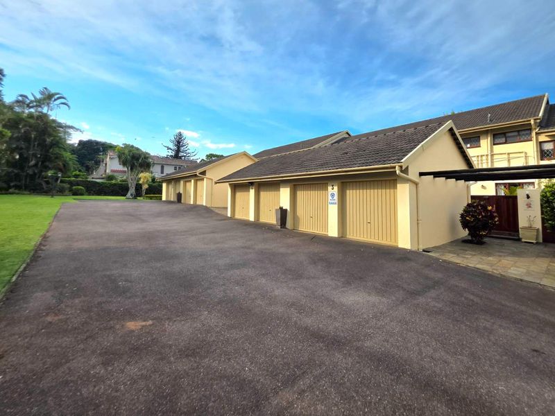 A row of residential garages with tiled roofs and paved driveway access, situated within a well-maintained townhouse complex.