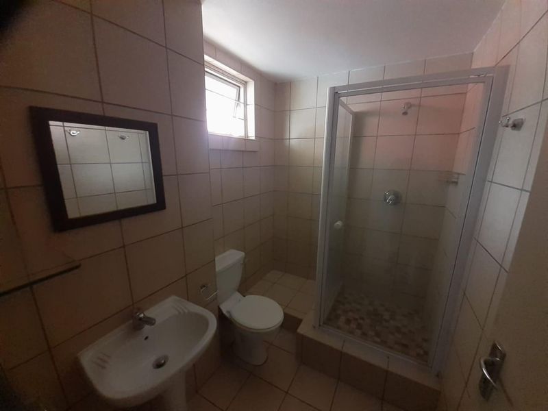 A functional bathroom featuring a pedestal basin, toilet, and a glass-enclosed shower with tiled walls and flooring.