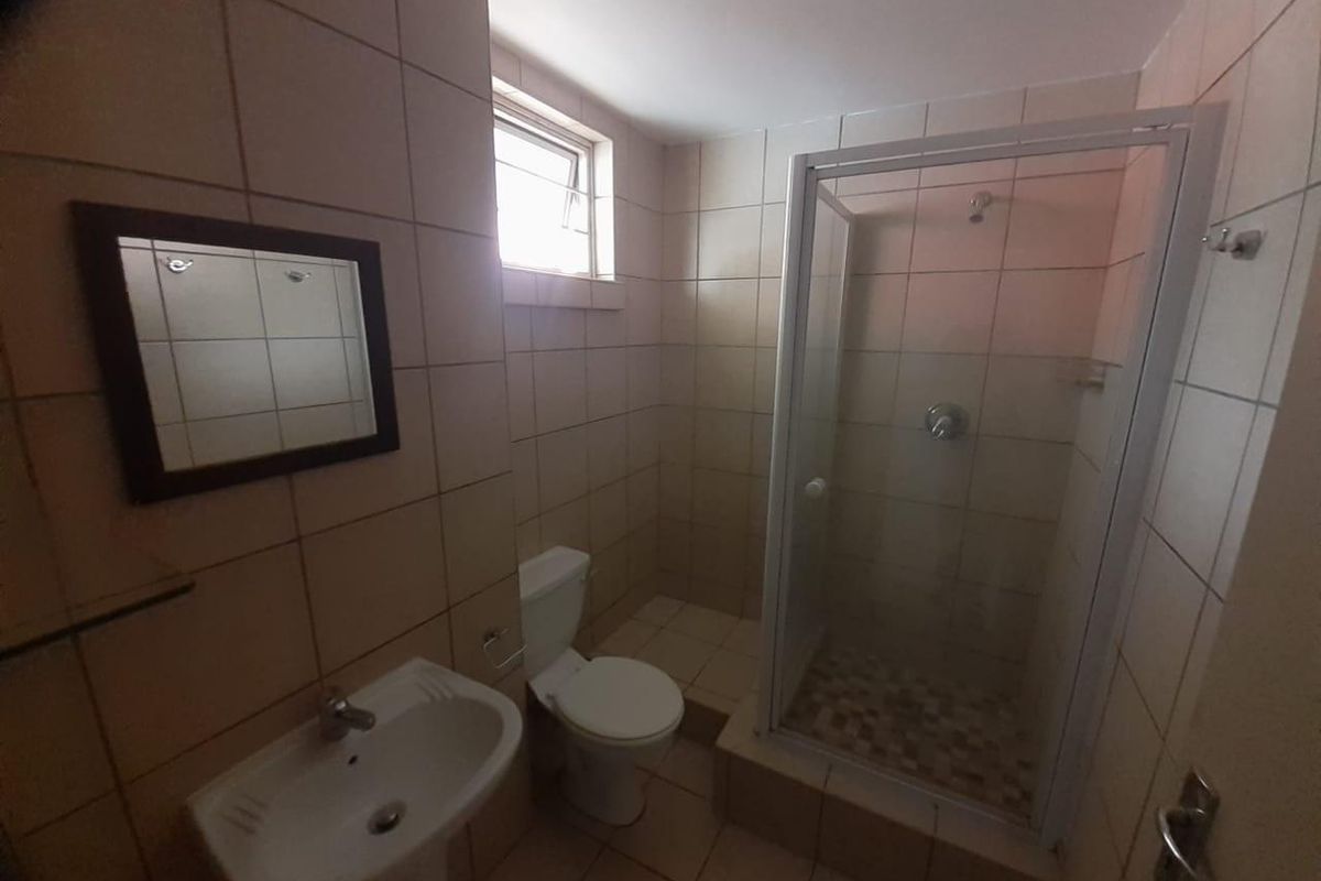 A functional bathroom featuring a pedestal basin, toilet, and a glass-enclosed shower with tiled walls and flooring.
