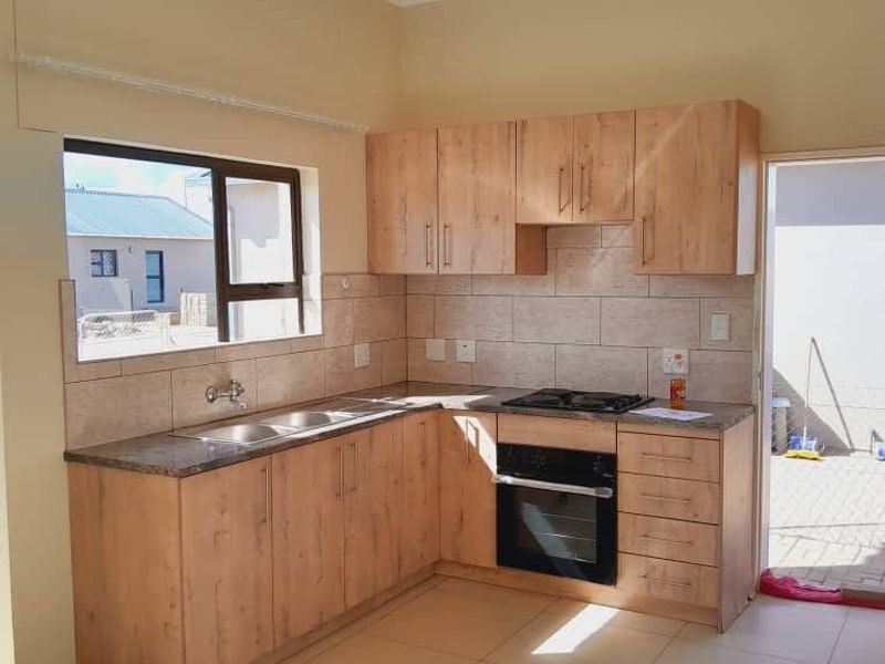 A clean, functional kitchen featuring light wood-look cabinetry, granite countertops, a built-in oven, gas hob, and neutral tiled flooring.