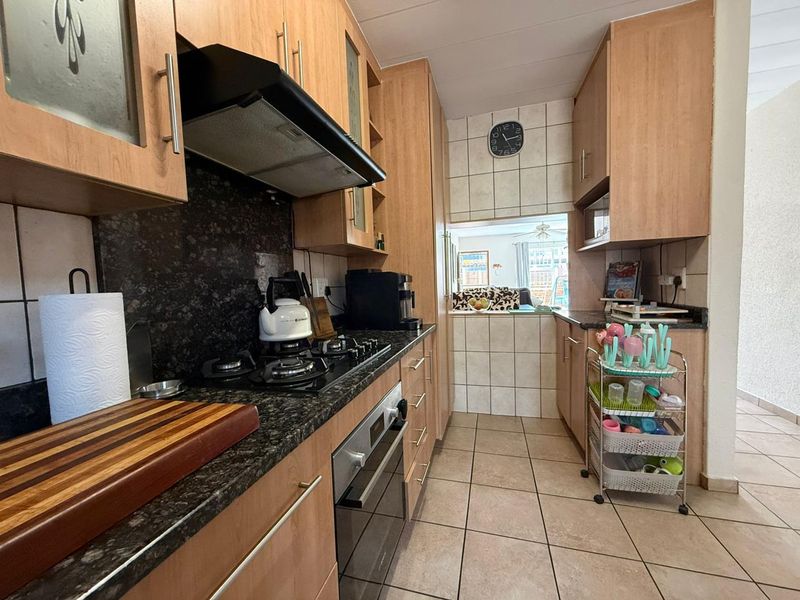 A functional kitchen featuring wood-finish cabinetry, granite countertops, a gas hob with extractor fan, and tiled flooring, with a pass-through window to the living area.
