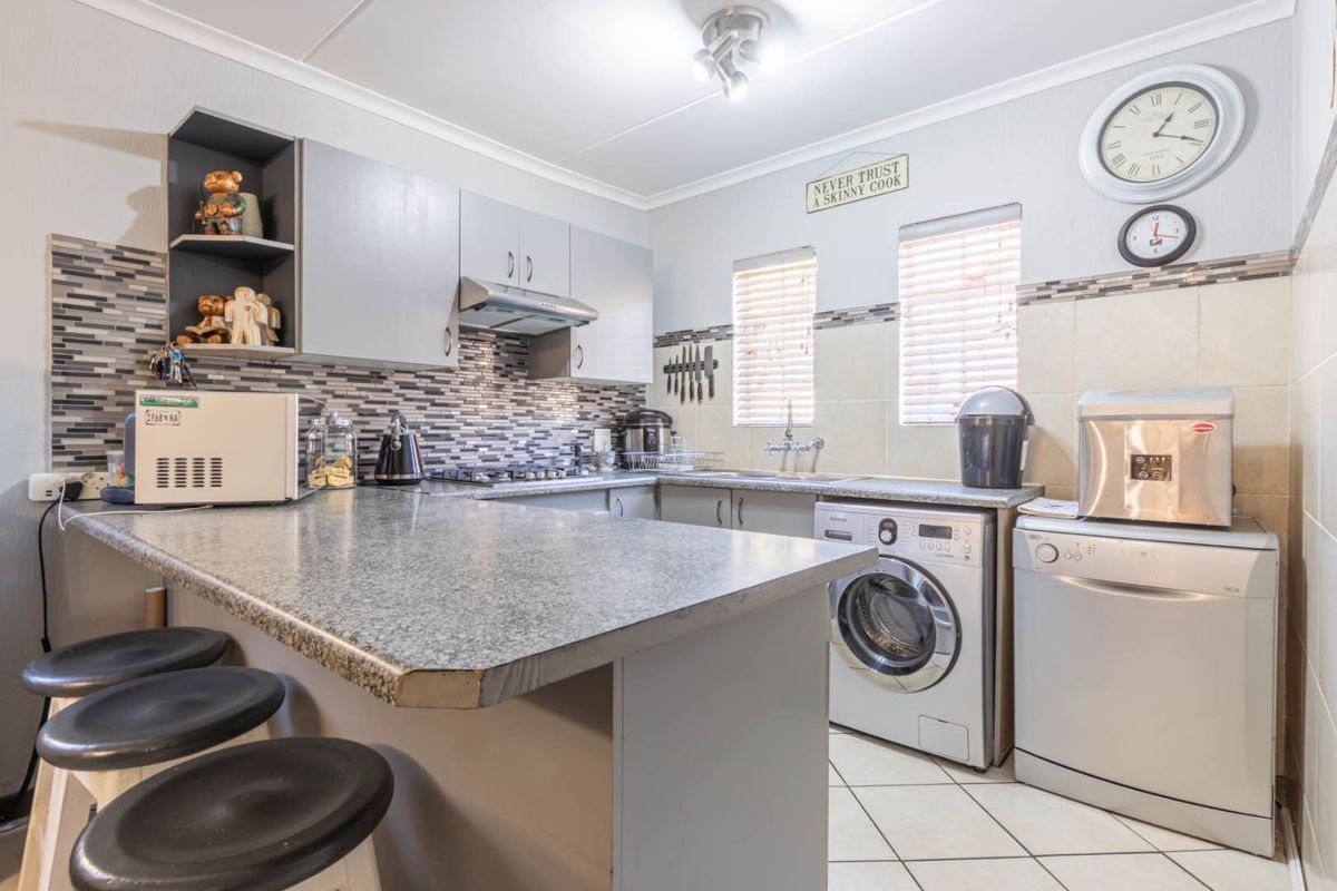 Functional kitchen featuring grey cabinetry, granite-look countertops, mosaic tile backsplash, integrated hob, extractor fan, and dedicated space for laundry and dishwasher appliances.