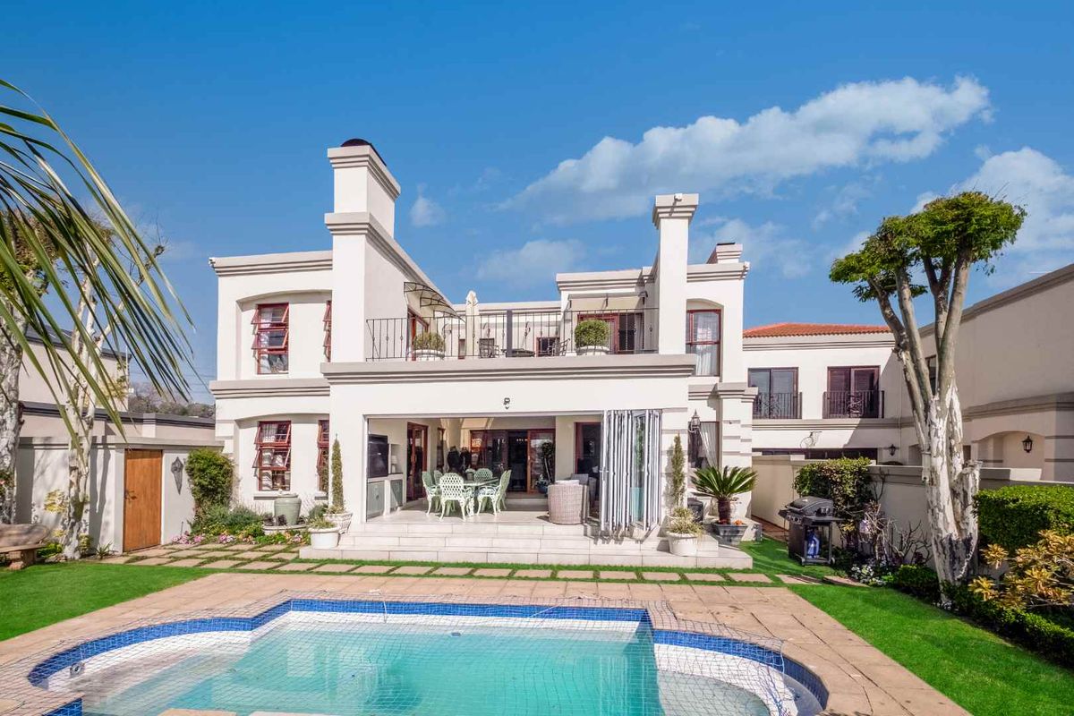 Rear view of a multi-story residence featuring a swimming pool, paved patio area, and an upper-level balcony with architectural chimneys.