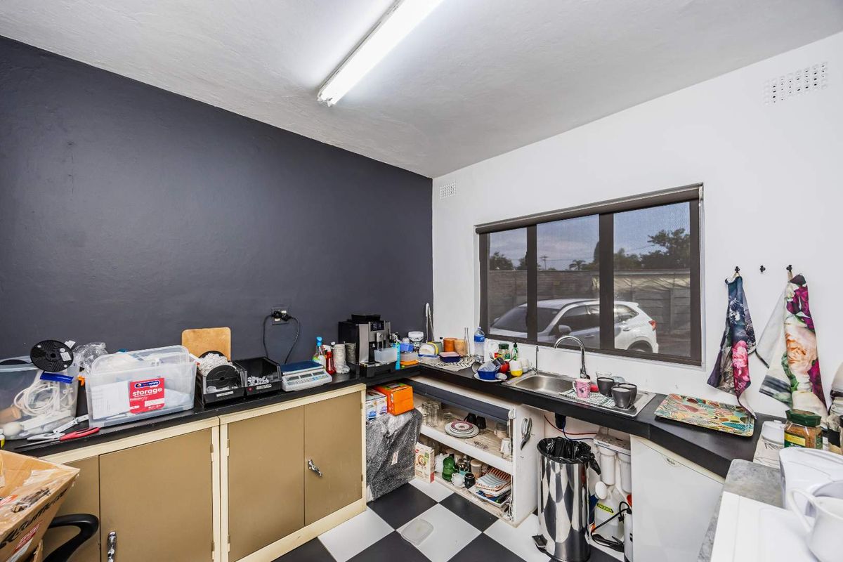 A functional kitchenette area featuring dark countertops, built-in cabinetry, a stainless steel sink, and a checkered floor finish.