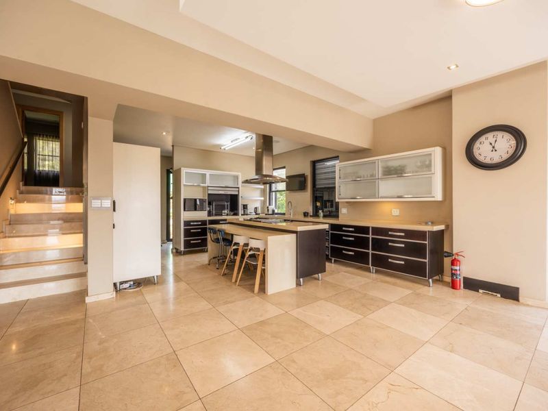 Spacious open-plan kitchen featuring a central island, modern cabinetry, and stone flooring, seamlessly connected to a staircase leading to the upper level.