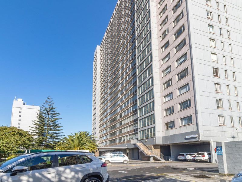 Exterior view of a multi-story apartment building featuring a paved parking area and concrete structural elements.