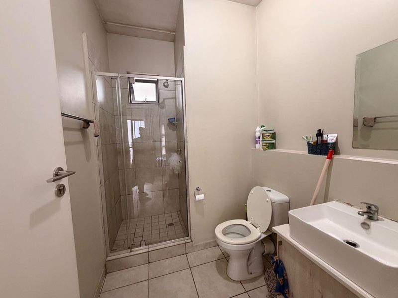 A functional bathroom featuring a glass-enclosed shower, a standard toilet, and a modern vessel-style vanity basin with a wall-mounted mirror.