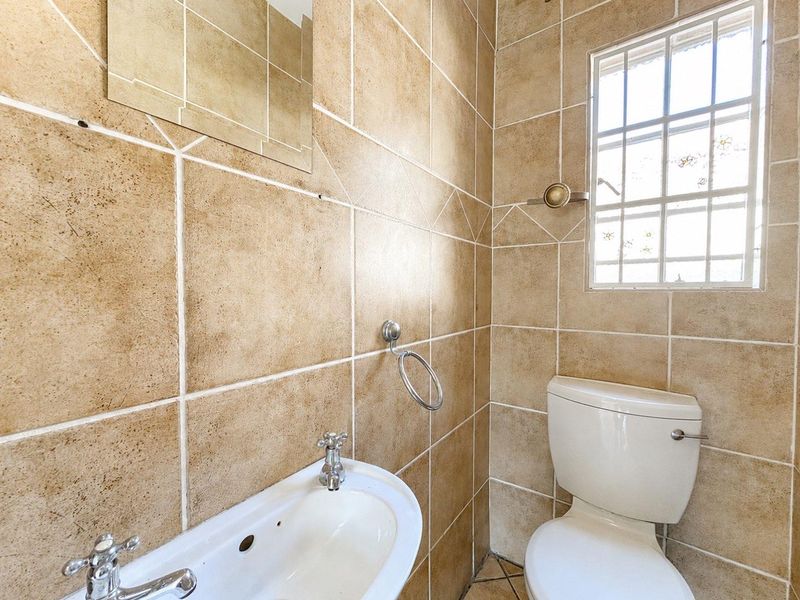 A compact bathroom featuring floor-to-ceiling ceramic tiling, a pedestal basin with chrome fixtures, and a standard toilet.