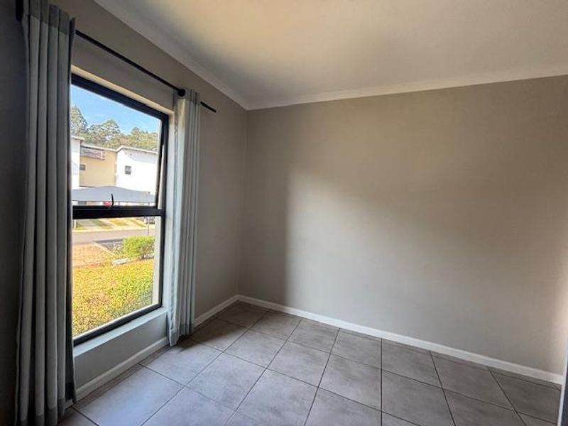 A bright, empty bedroom featuring neutral wall tones, tiled flooring, and a large window with installed curtain rods.