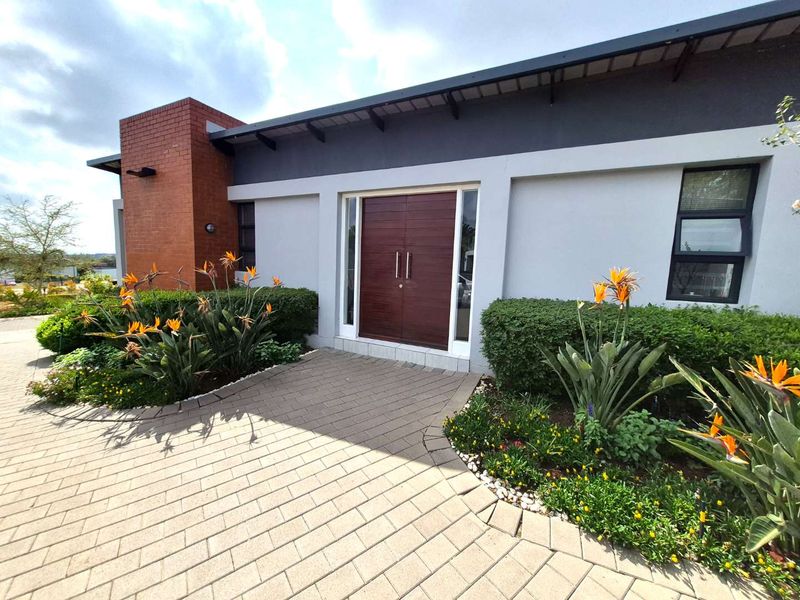 Modern townhouse entrance featuring a double wooden door, brick architectural detailing, and a neatly paved walkway surrounded by established garden beds.