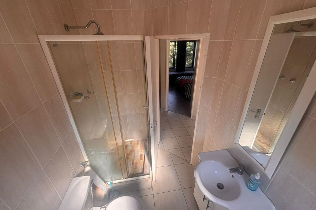 A functional bathroom featuring a glass-enclosed shower, a vanity basin with storage, and neutral wall and floor tiling.