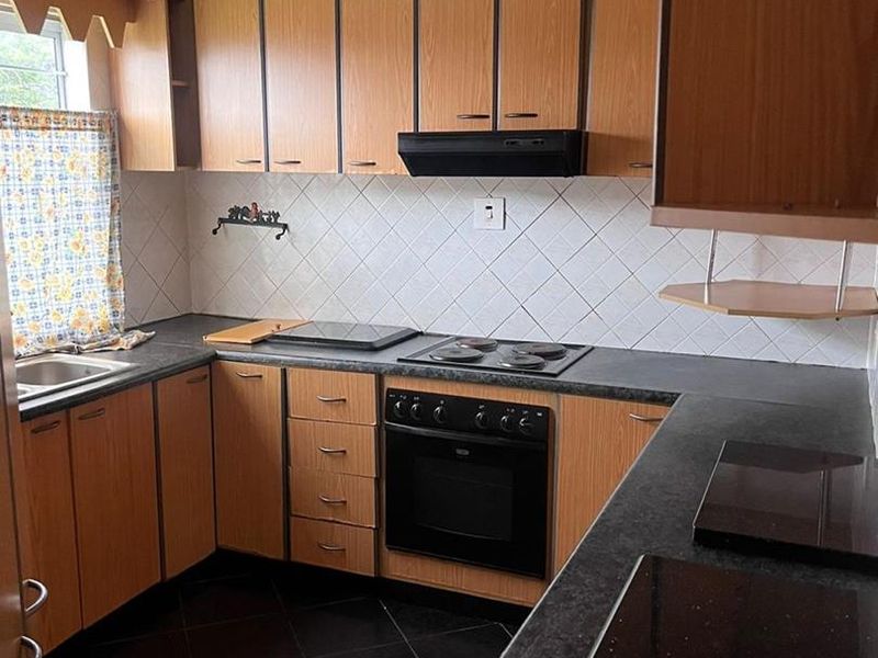 A functional kitchen featuring wood-look cabinetry, dark laminate countertops, a built-in oven with hob, and a tiled backsplash.