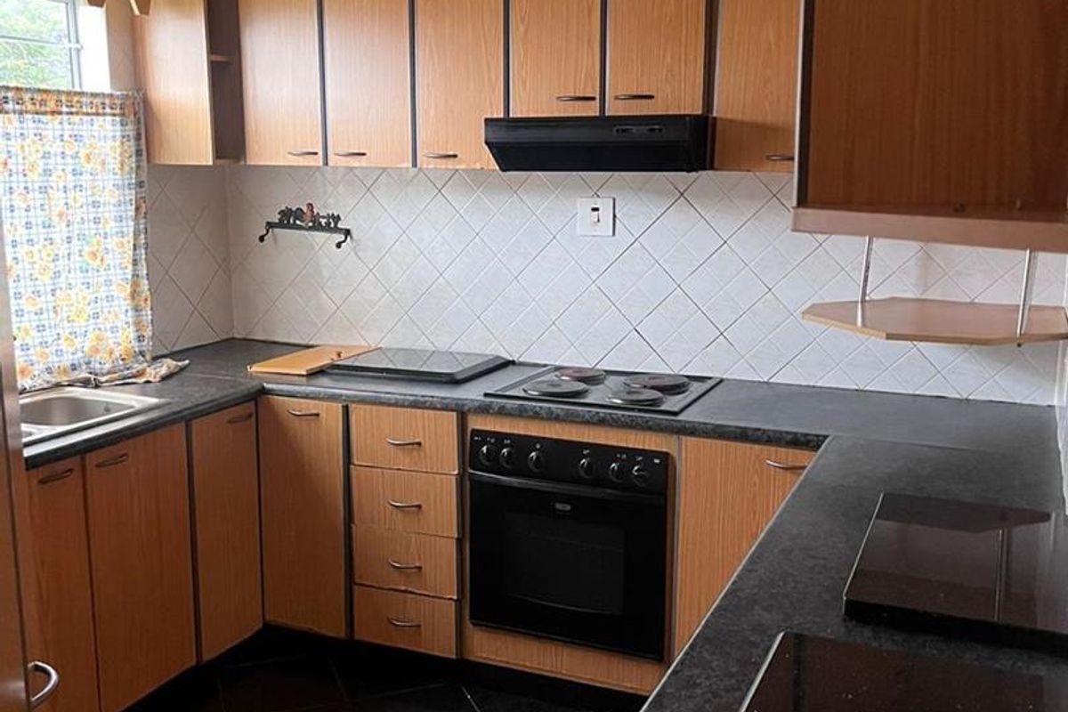 A functional kitchen featuring wood-look cabinetry, dark laminate countertops, a built-in oven with hob, and a tiled backsplash.