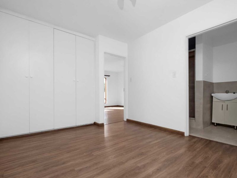 A bright, empty bedroom featuring laminate flooring, built-in cupboards, and direct access to an en-suite bathroom.
