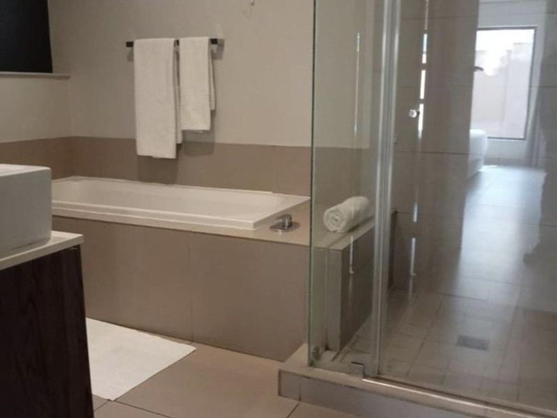 Modern bathroom featuring a built-in bathtub, a separate glass-enclosed shower, and a vanity unit with a basin, finished with neutral floor tiles.