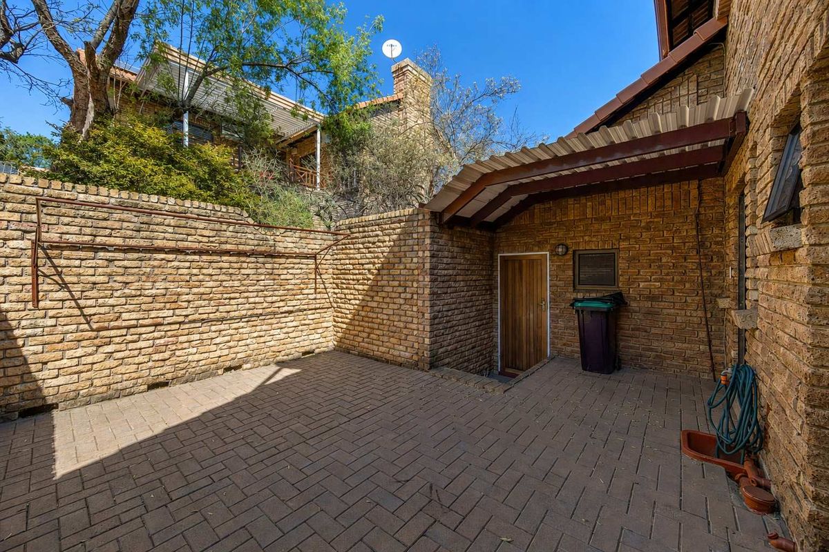 A private rear courtyard featuring brick paving, a covered patio area, and high brick boundary walls for added privacy.