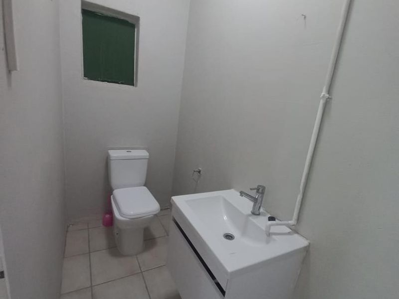 A compact, functional bathroom featuring a wall-mounted vanity, basin, and toilet with tiled flooring and exposed surface-mounted plumbing.
