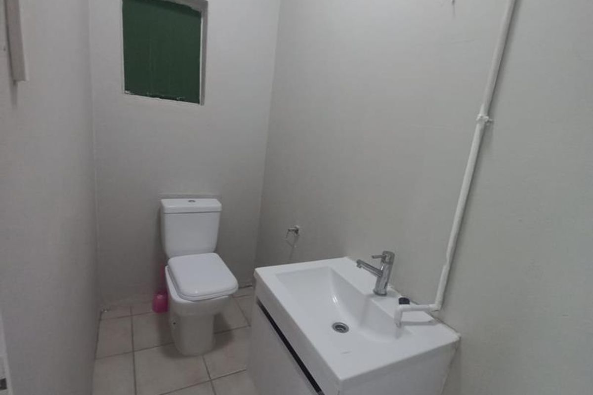 A compact, functional bathroom featuring a wall-mounted vanity, basin, and toilet with tiled flooring and exposed surface-mounted plumbing.