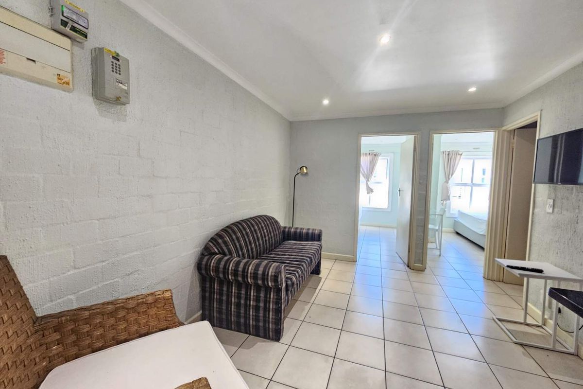A living area featuring tiled flooring, recessed ceiling lighting, and direct access to adjacent bedrooms.