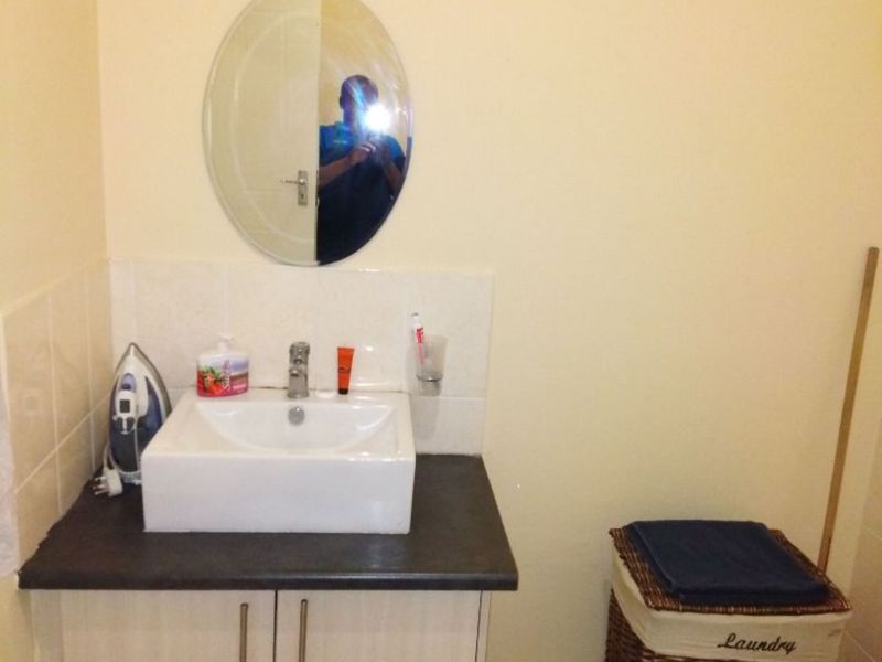 A functional bathroom featuring a modern square basin, vanity cabinet with dark countertop, and a wall-mounted oval mirror.