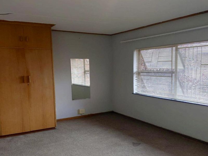 A vacant bedroom featuring built-in wooden cupboards, carpeted flooring, and venetian blinds, offering a blank canvas for renovation.