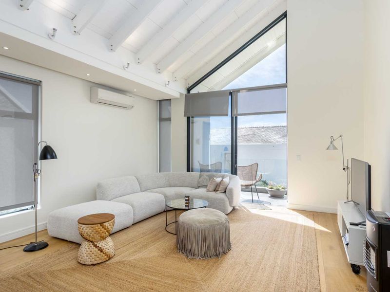 Bright living room featuring a high vaulted ceiling with exposed beams, timber flooring, and large glass sliding doors leading to an outdoor area.