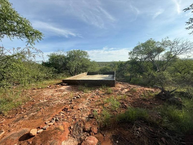 An elevated view of a concrete foundation and brick masonry base situated on a natural rocky landscape within a rural farm setting.